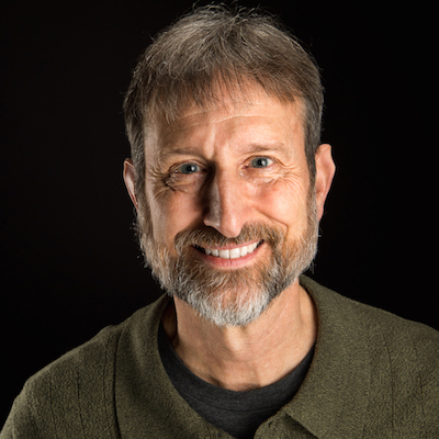 Smiling man with short hair and beard in a green sweater.