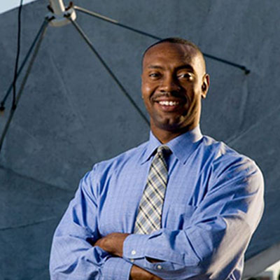 Person in a blue shirt standing in front of a large satellite dish.