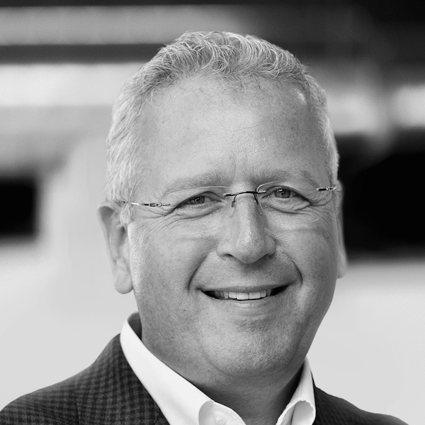 Portrait of a smiling man with glasses in a suit, in black and white.