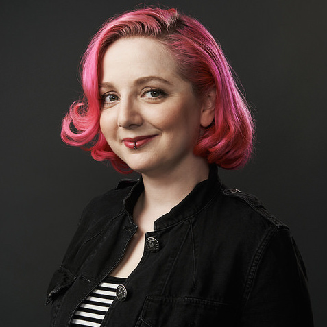 Person with pink hair wearing a black jacket against a dark background.