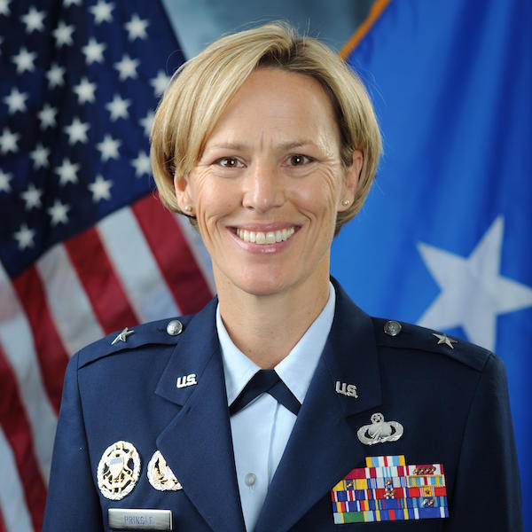 U.S. Air Force officer in uniform smiling in front of flags.