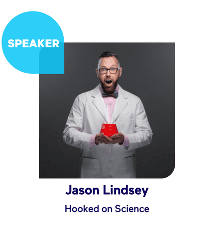 Speaker in a lab coat holding a red beaker, excited expression