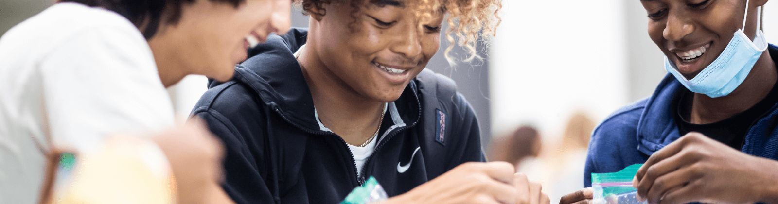 Three teenagers smiling and interacting with materials in a group activity.