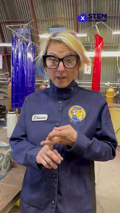 Person in welding gear explaining STEM concepts in an industrial setting.