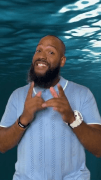 Man gesturing underwater, wearing a light blue shirt.