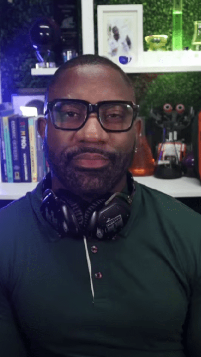 Person with glasses and headphones sitting in a tech-themed room.