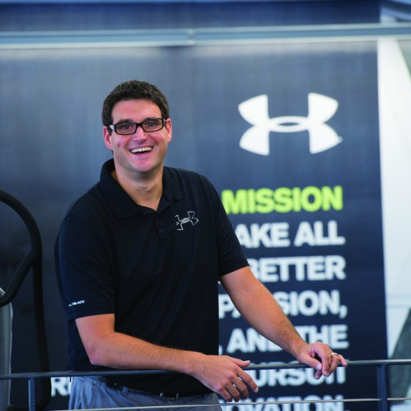 Smiling man in front of Under Armour mission statement wall.