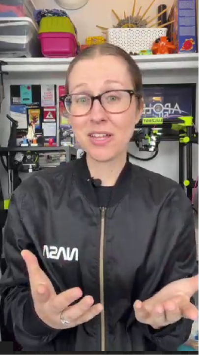 Person in a NASA jacket in a workshop setting with 3D printers.