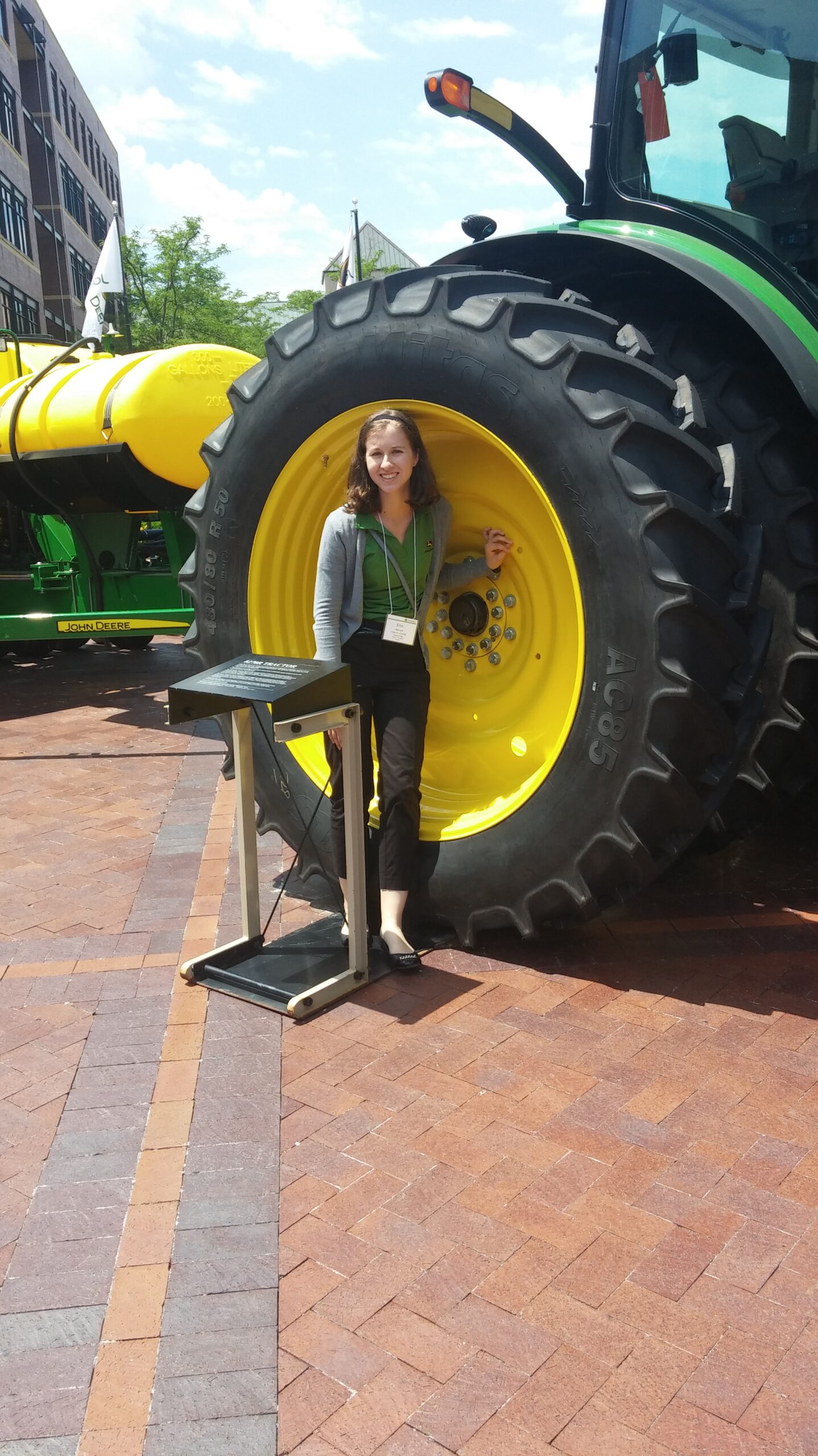 Woman standing next to a large tractor wheel displayed outdoors.