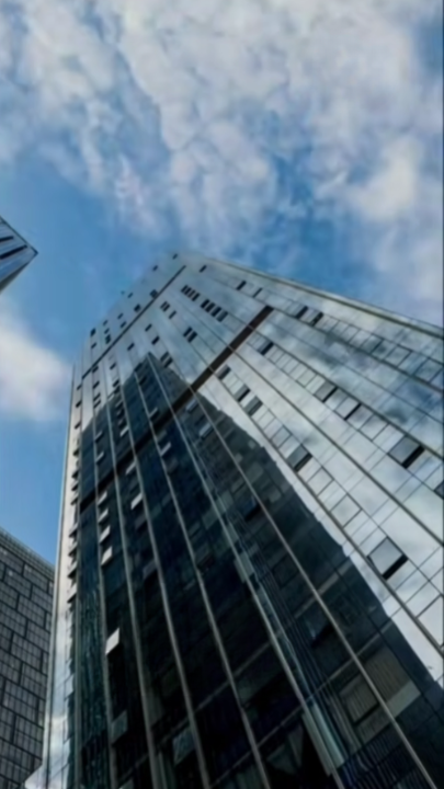 Tall glass buildings reflecting the sky with scattered clouds.