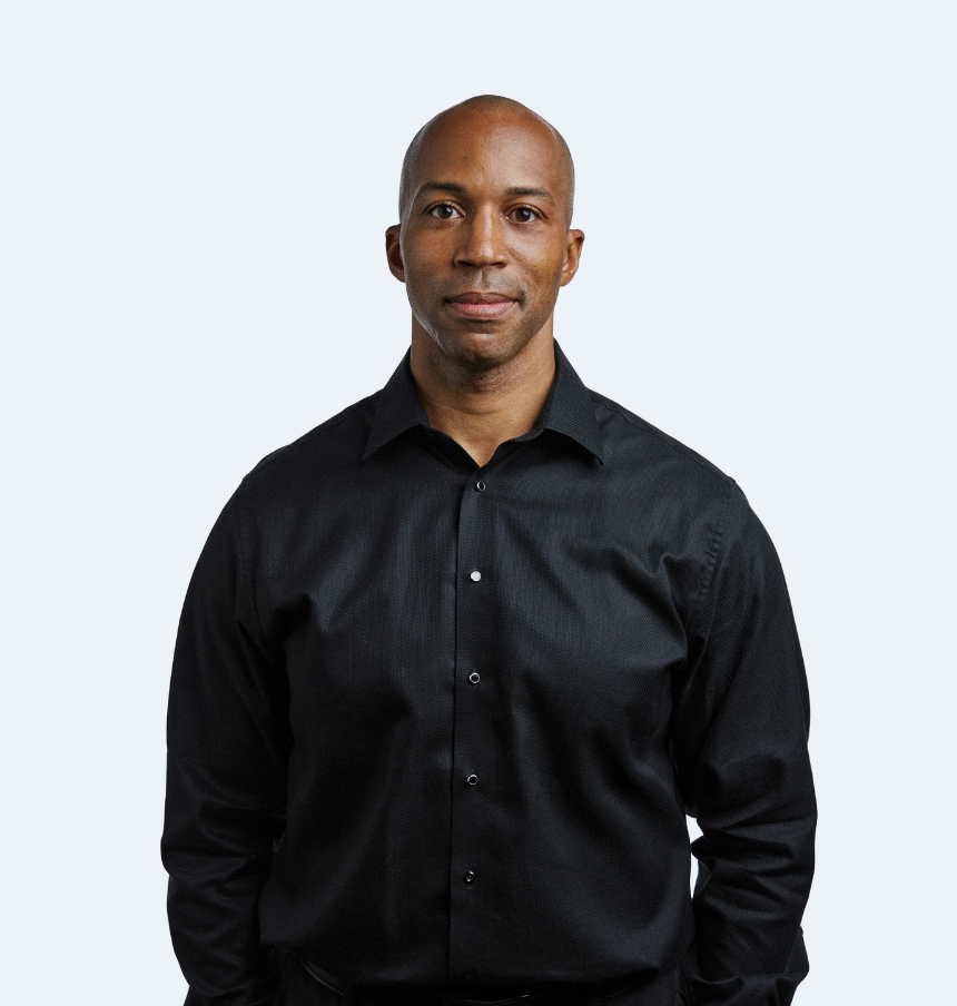 Man in black shirt standing against a plain background.