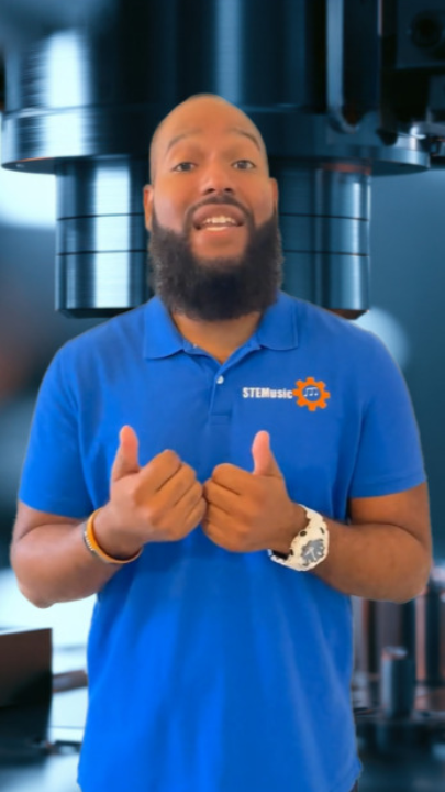 Man in blue shirt speaking in front of industrial machinery.