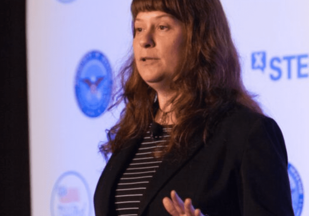 Woman speaking at STEM event with backdrop of educational logos.