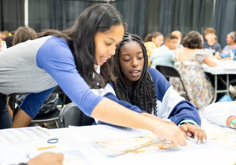 Two young women collaborating intently on a project sheet.