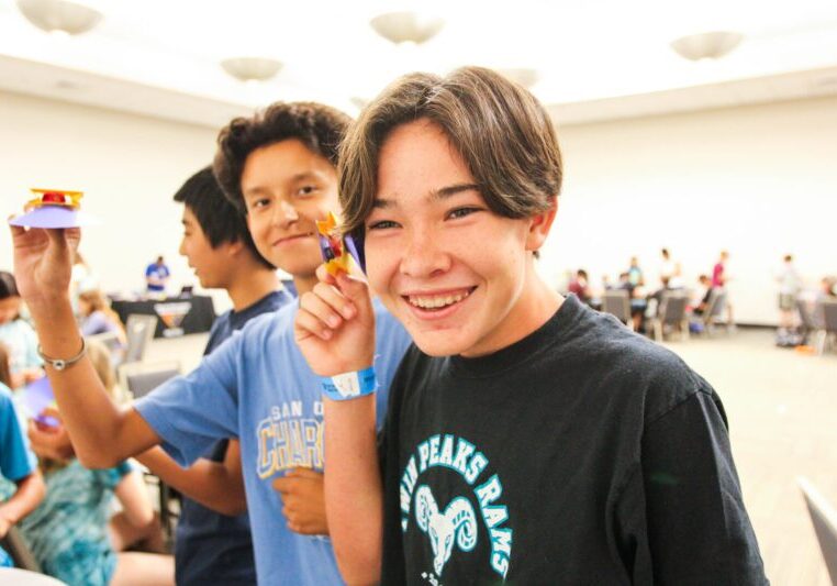 Happy students displaying small projects at an indoor event.