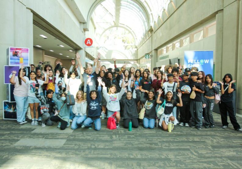 Large diverse group of students enthusiastically waving indoors.