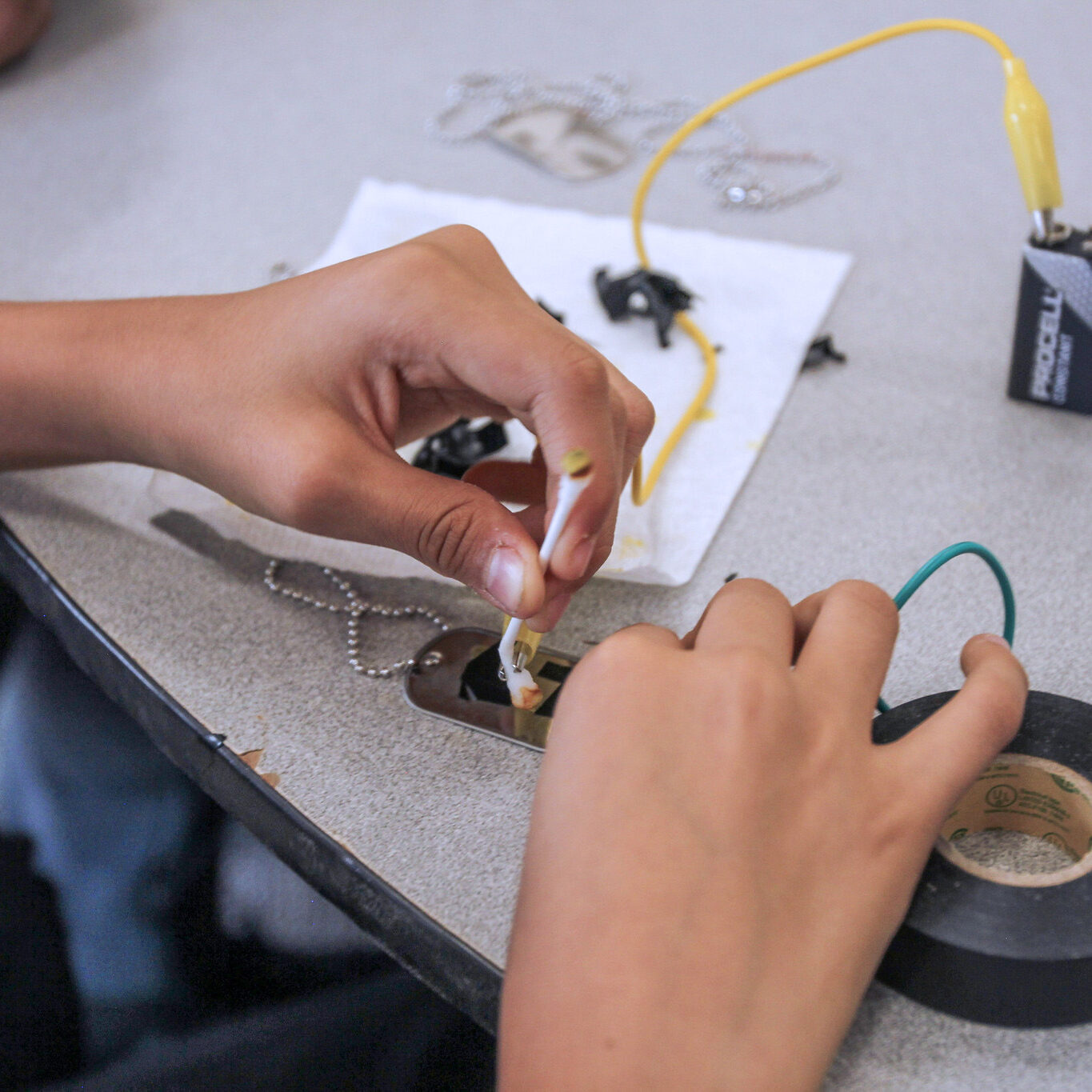 Hands working on a small electronics project with a battery and wires.