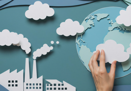 Papercut of a hand holding a globe with clouds and factory.