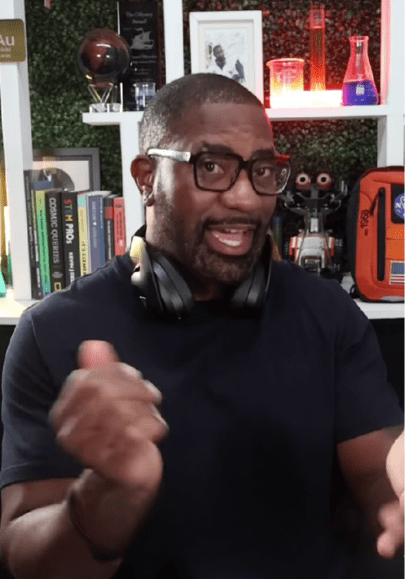 Person speaking in front of a science-themed backdrop with books and lab equipment.