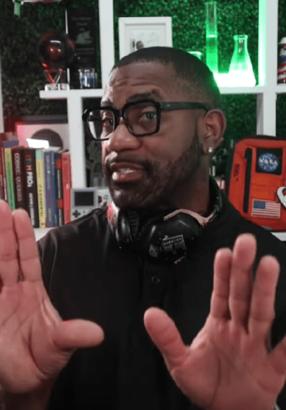 Man in a tech-themed room gestures towards the camera