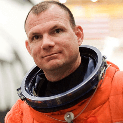 Man wearing an orange astronaut suit with a helmet in hand.
