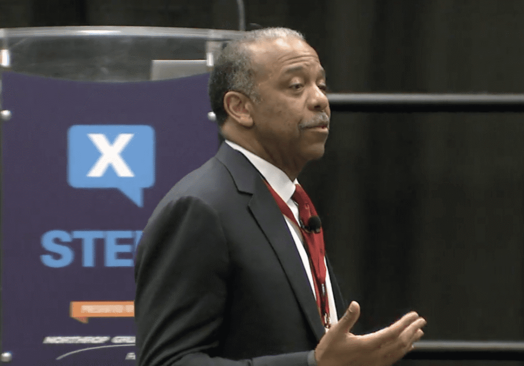 Man in a suit speaking at a podium with a STEM sign