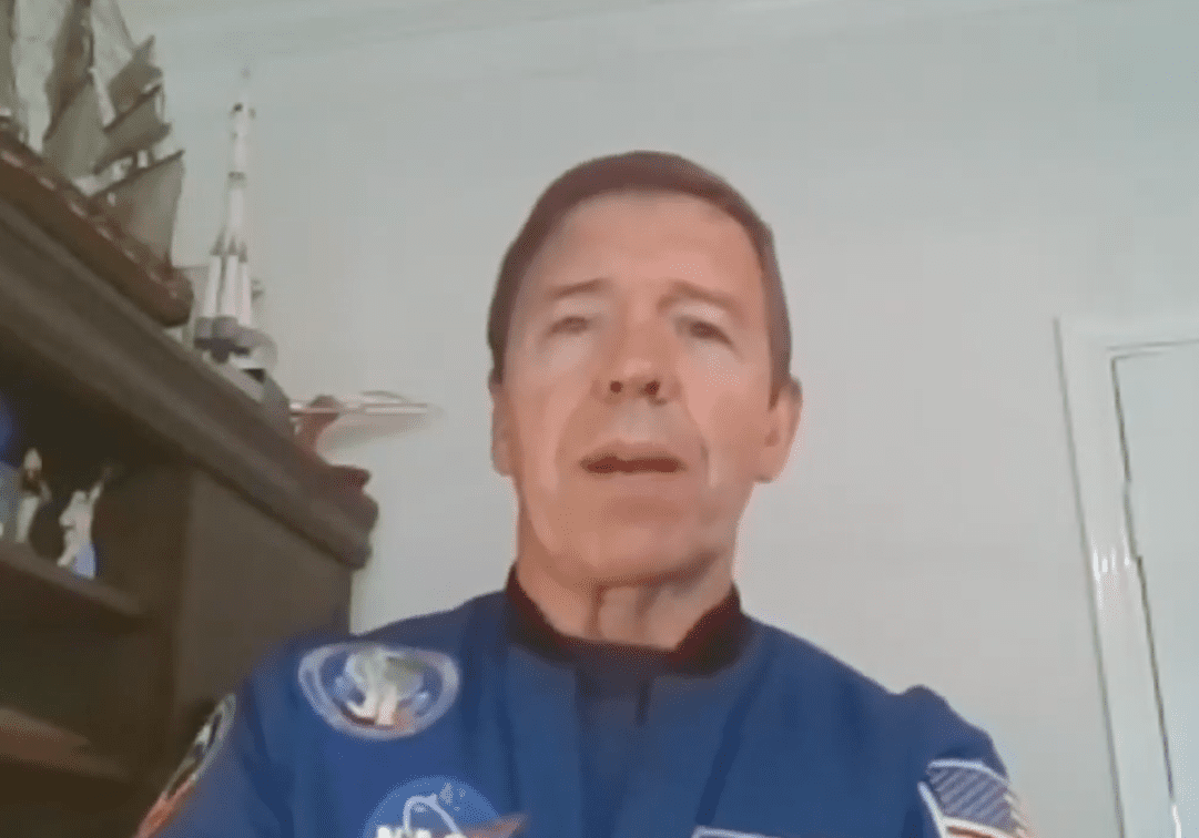 Person wearing a blue jacket with NASA patches, speaking indoors.