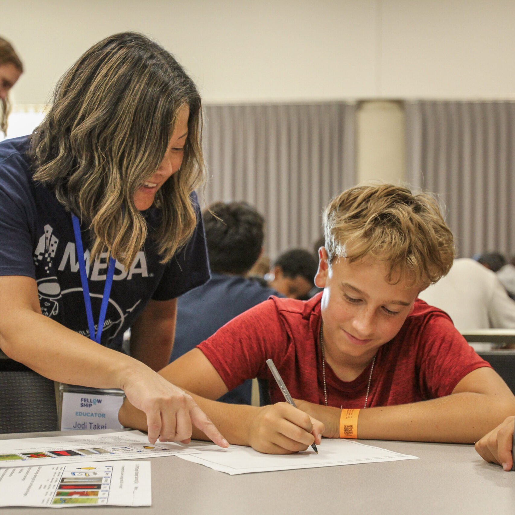 Educator assisting a student with a writing task in a classroom.