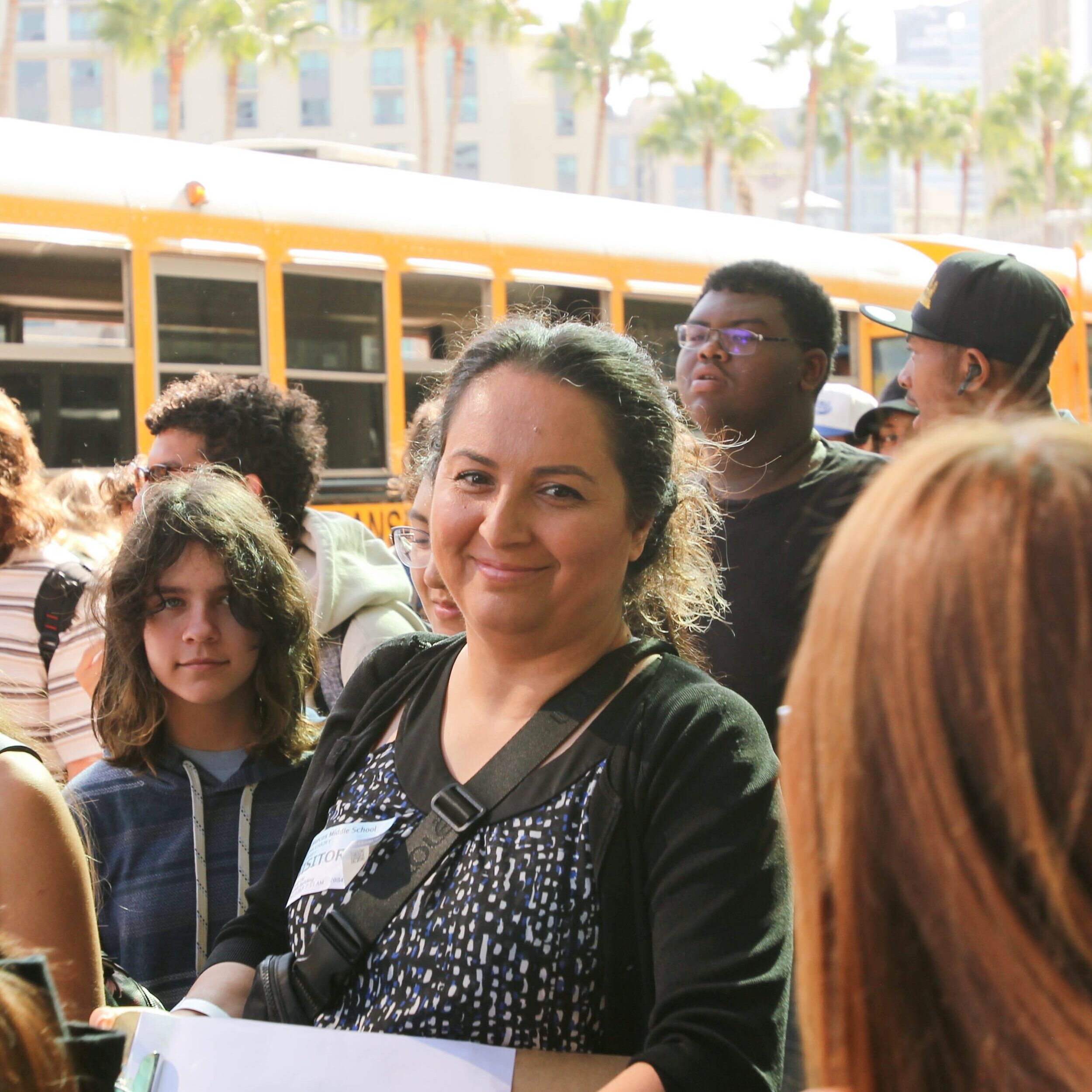 Smiling woman standing with students in front of a school bus.