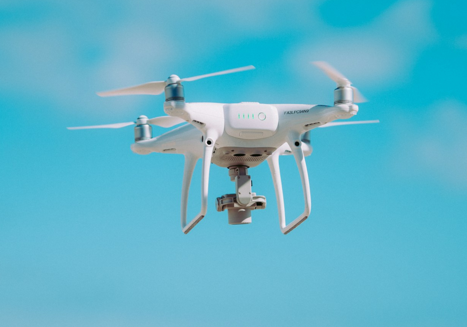 White drone flying against a clear blue sky background.
