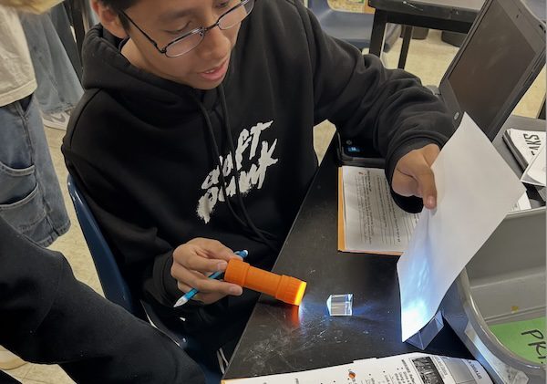 Student uses a flashlight and prism to project light onto paper during science class.