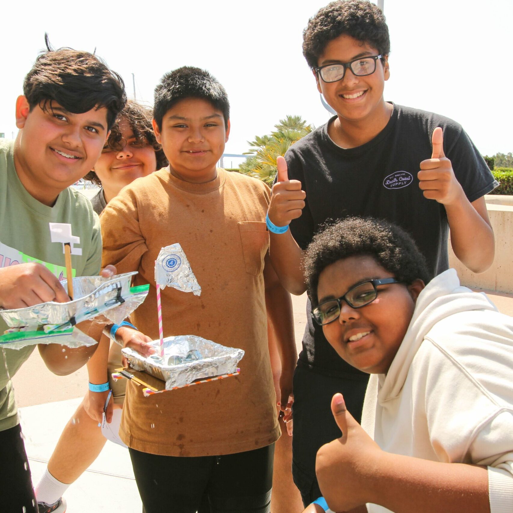 Five smiling students proudly displaying handmade foil boats.