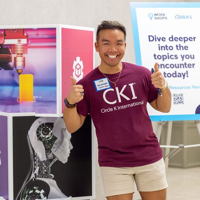 Man in CKI shirt posing by 3D printing and robotics display.