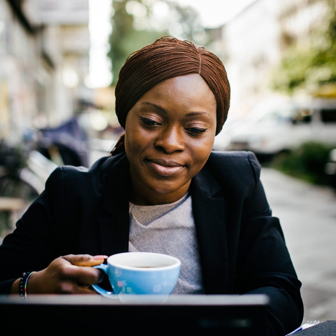 Black woman drinking coffee while working on a laptop.