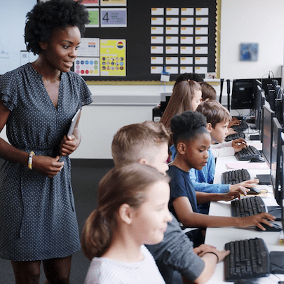 Teacher assists students working at computers in a classroom setting.