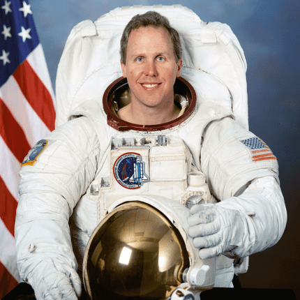 Astronaut in a space suit posing in front of an American flag.