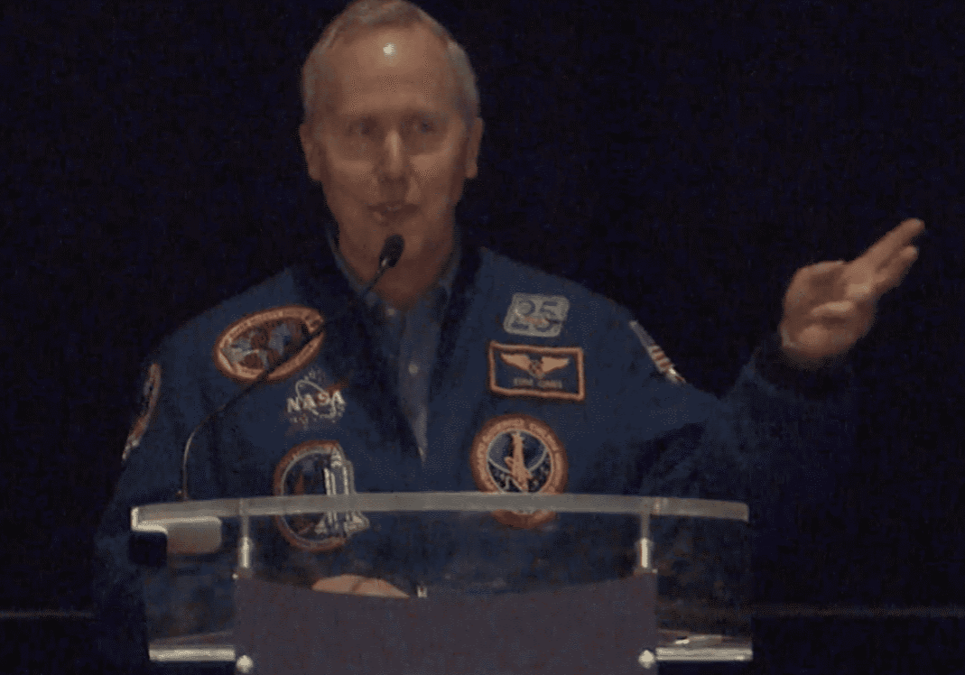 Person in NASA jacket speaking at a podium.