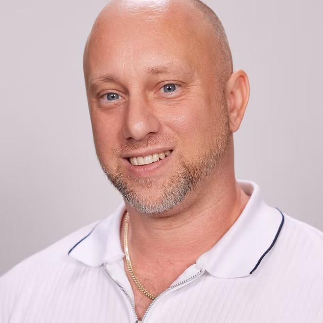 Smiling man wearing white polo shirt.