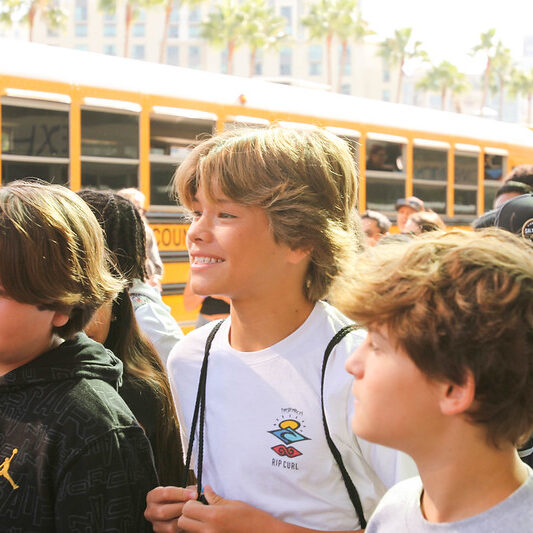 Group of young attendees at an outdoor workshop near school buses.