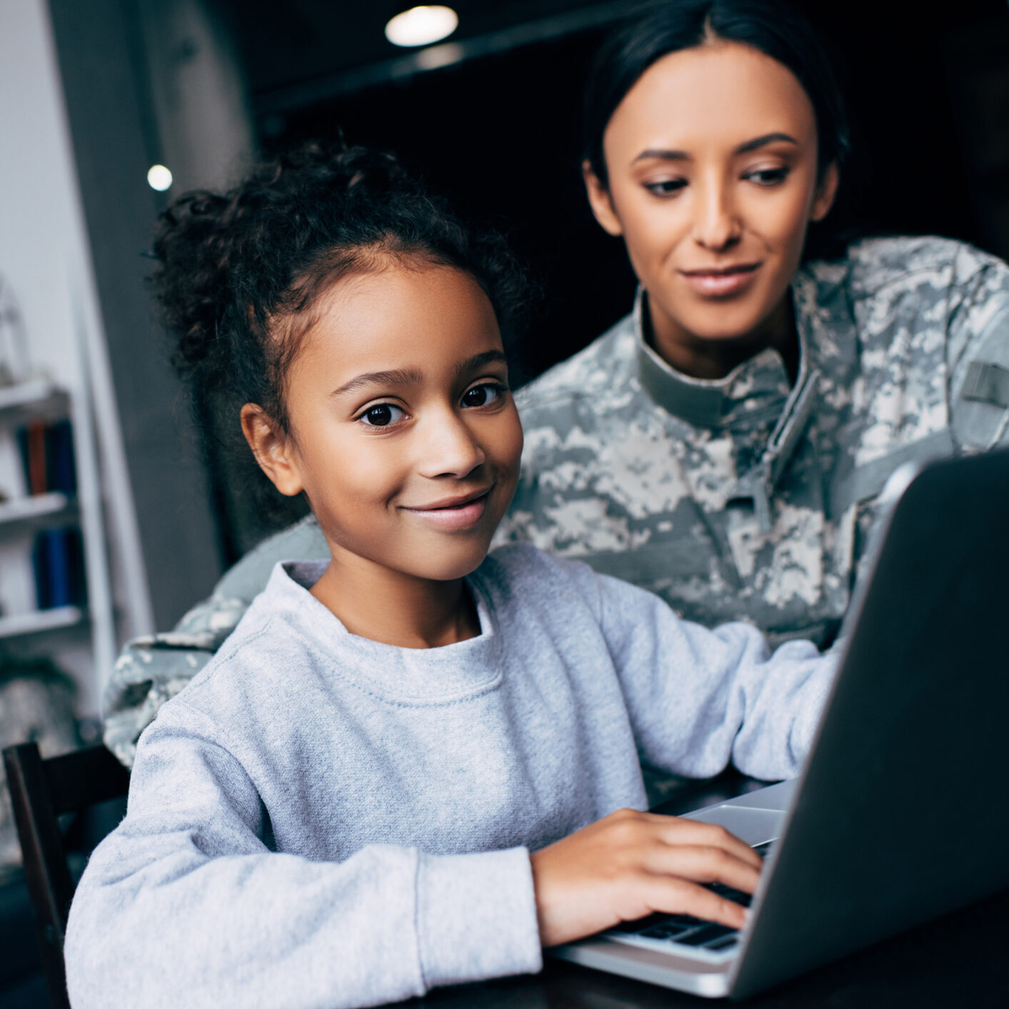 Mother in military uniform using laptop with her daughter at home