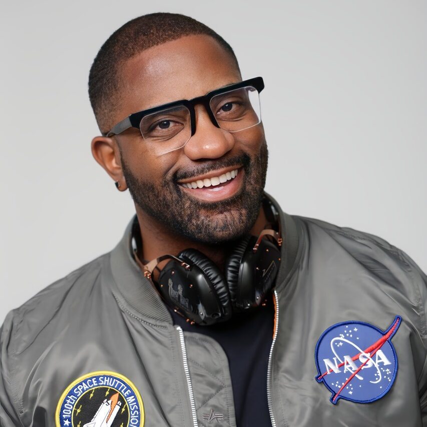 Maynard smiling in a NASA bomber jacket and headphones.